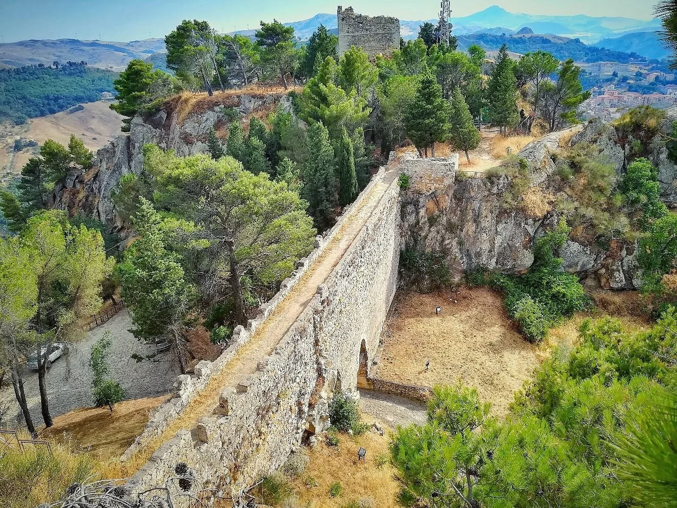 The stone bridge of the Castle of Nicosia linking the twin rocky peaks; on the left summit the Norman tower ruin, with the inland Sicilian panorama in the background