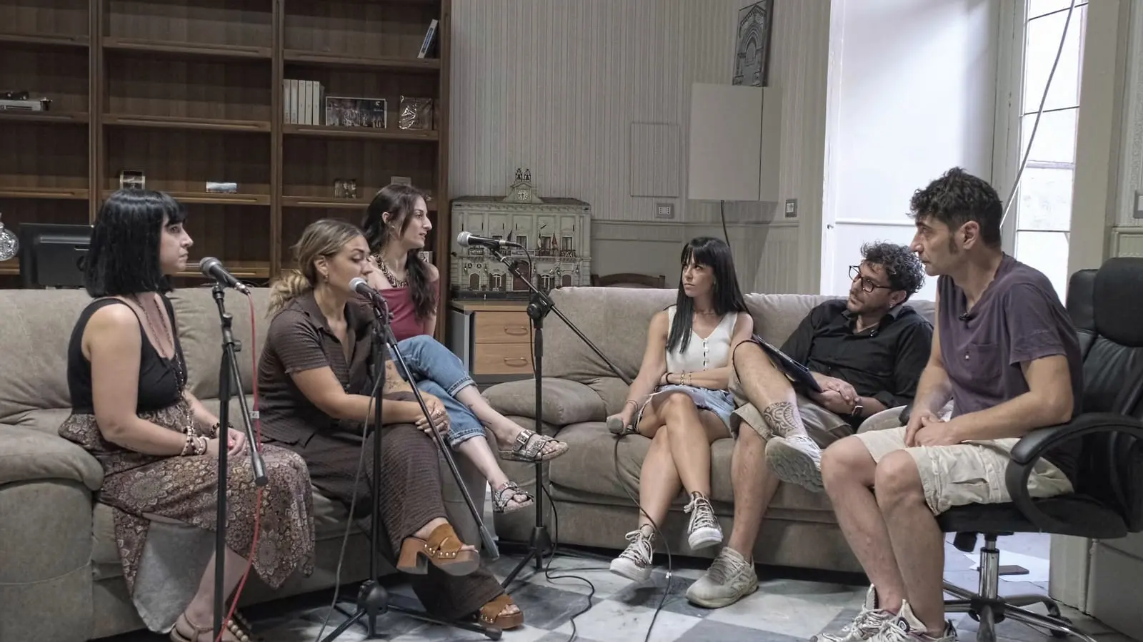 La registrazione della quarta puntata, nella sala con la libreria di legno e il pavimento a scacchi: sei persone sedute in cerchio, cinque sul divano e una su una poltrona da ufficio, fra microfoni ad asta e cavi a terra.