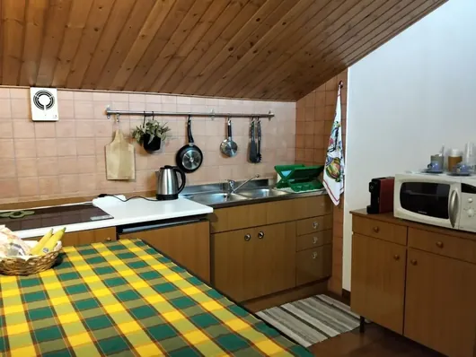 Cucina con piano cottura, lavello, pentole appese e microonde sotto soffitto in legno