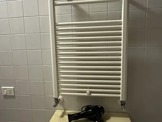 Bagno con termoarredo bianco a parete, piastrelle chiare e mobiletto con asciugacapelli