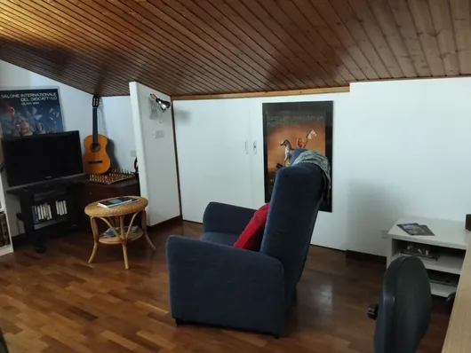 Soggiorno con soffitto in legno, due poltrone blu, televisore e chitarra appoggiata