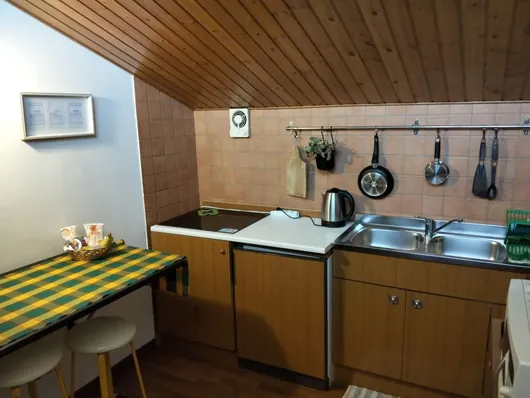 Angolo cucina con soffitto in legno, lavello doppio, pentole appese e tavolo con sgabelli